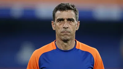 Middle-aged male coach, athletic build, mid-40s, short dark hair, focused expression, head-and-shoulders framed, wearing...