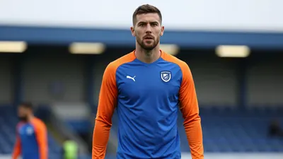 Mid-20s muscular defender, waist-up, face sharp and expressive, wearing an unmarked Eastleigh training shirt split blue...