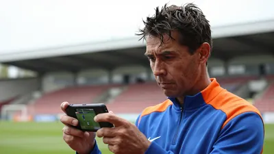 A close-up shot of a 35-year-old Eastleigh assistant coach, dressed in a plain blue and orange polyester training top...