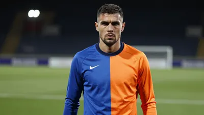 Mid-30s athletic striker, muscular torso, intense gaze, waist-up shot, wearing a plain training top split blue left side...