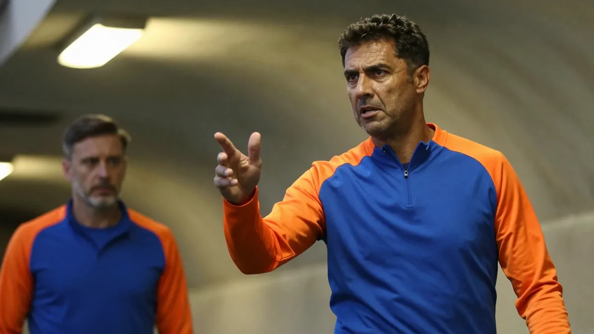 A 35-year-old Eastleigh coach, dressed in a plain unmarked blue and orange polyester training top, stands in the...