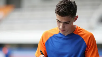 A young, athletic winger, 22, in a plain blue and orange training top, signs a contract, pen in hand, warm skin tones...